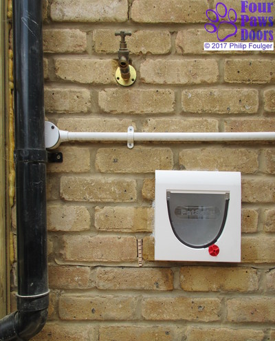 Cat flap fitted to wall between pipes